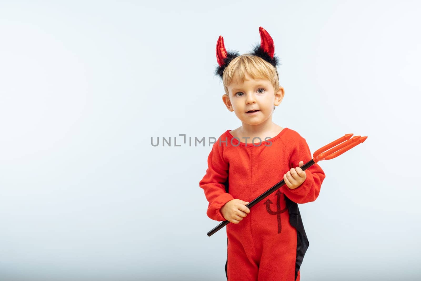 Happy cheerful boy in devil costume with trident on blue background. Halloween party concept. Web banner.