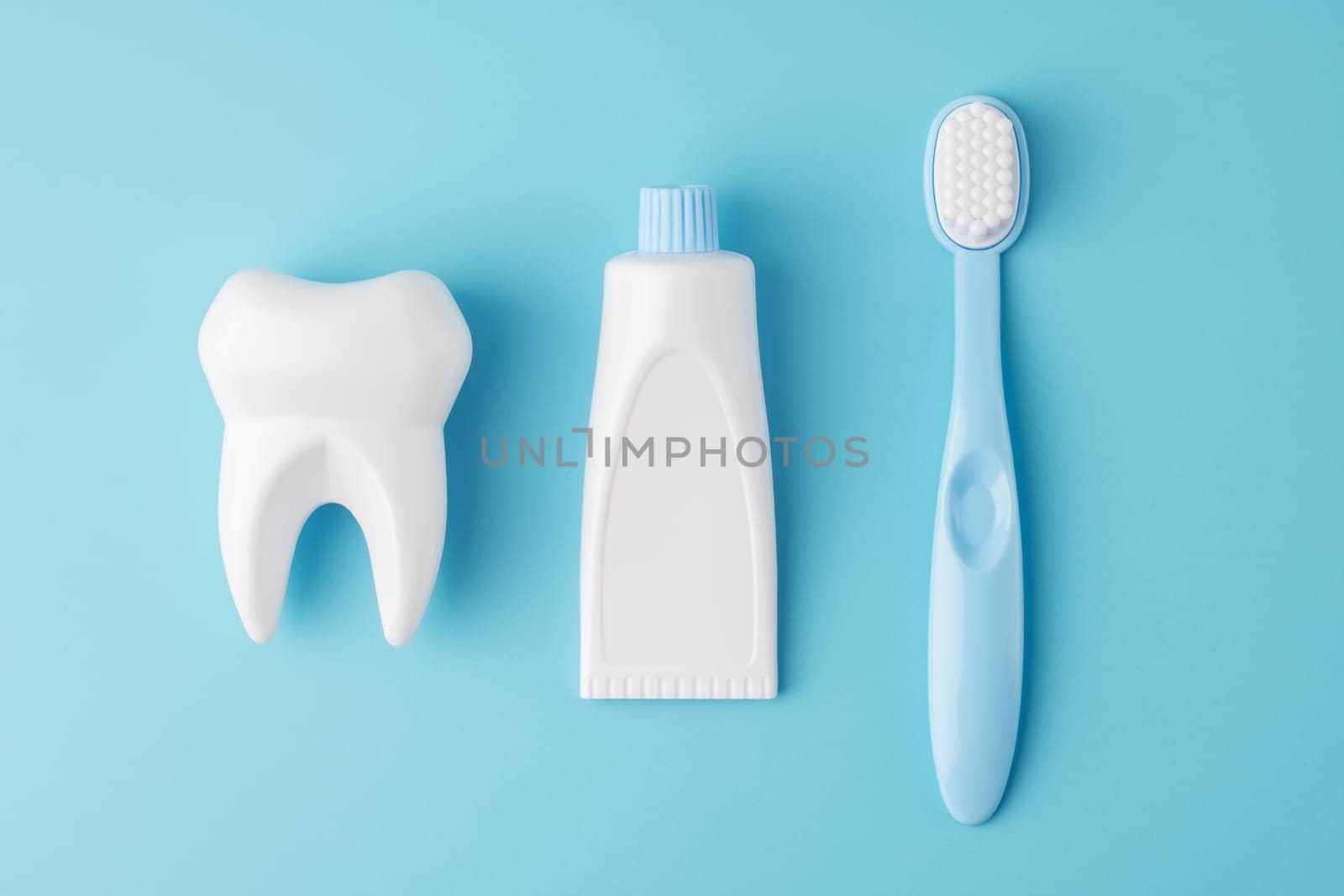 Teeth care and dental hygiene. Toy tooth, toothbrush with tube of toothpaste on blue background, flat lay. Dental concept.