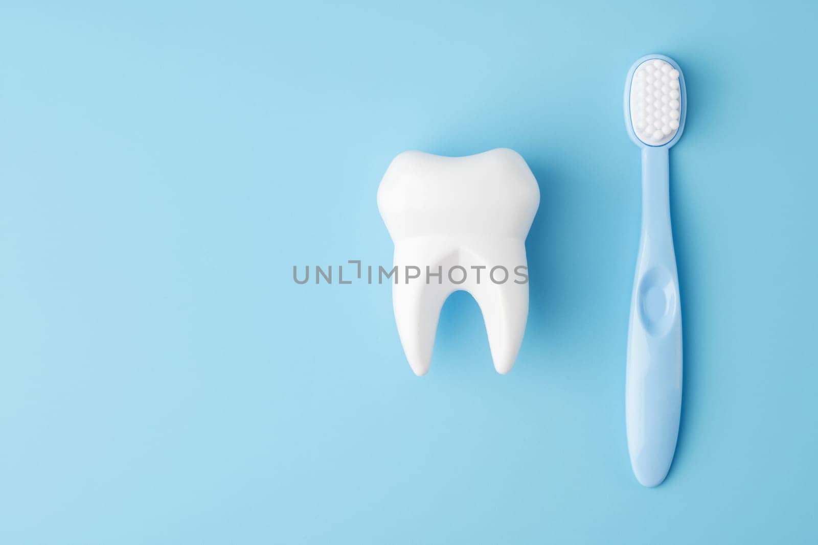 Teeth care and dental hygiene. Toy tooth and toothbrush on blue background, flat lay. Dental concept.
