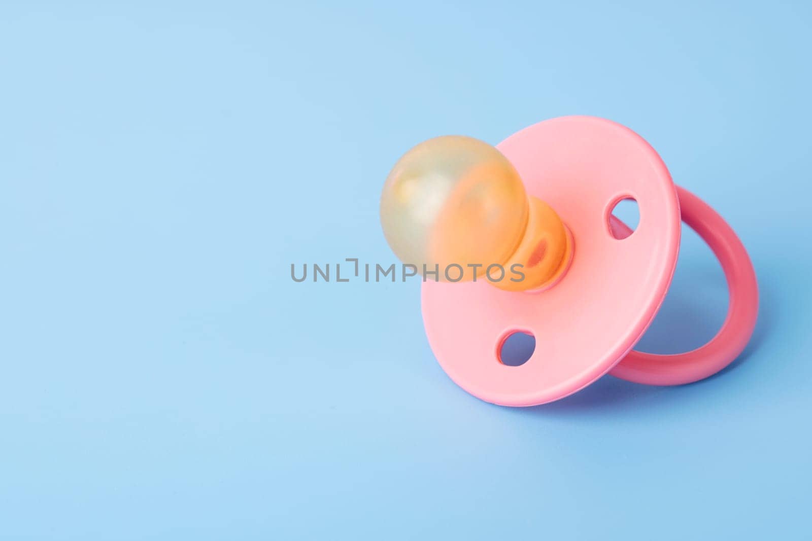 Orthodontic pacifier on a blue background. Pink baby pacifier on a blue background, space for text.