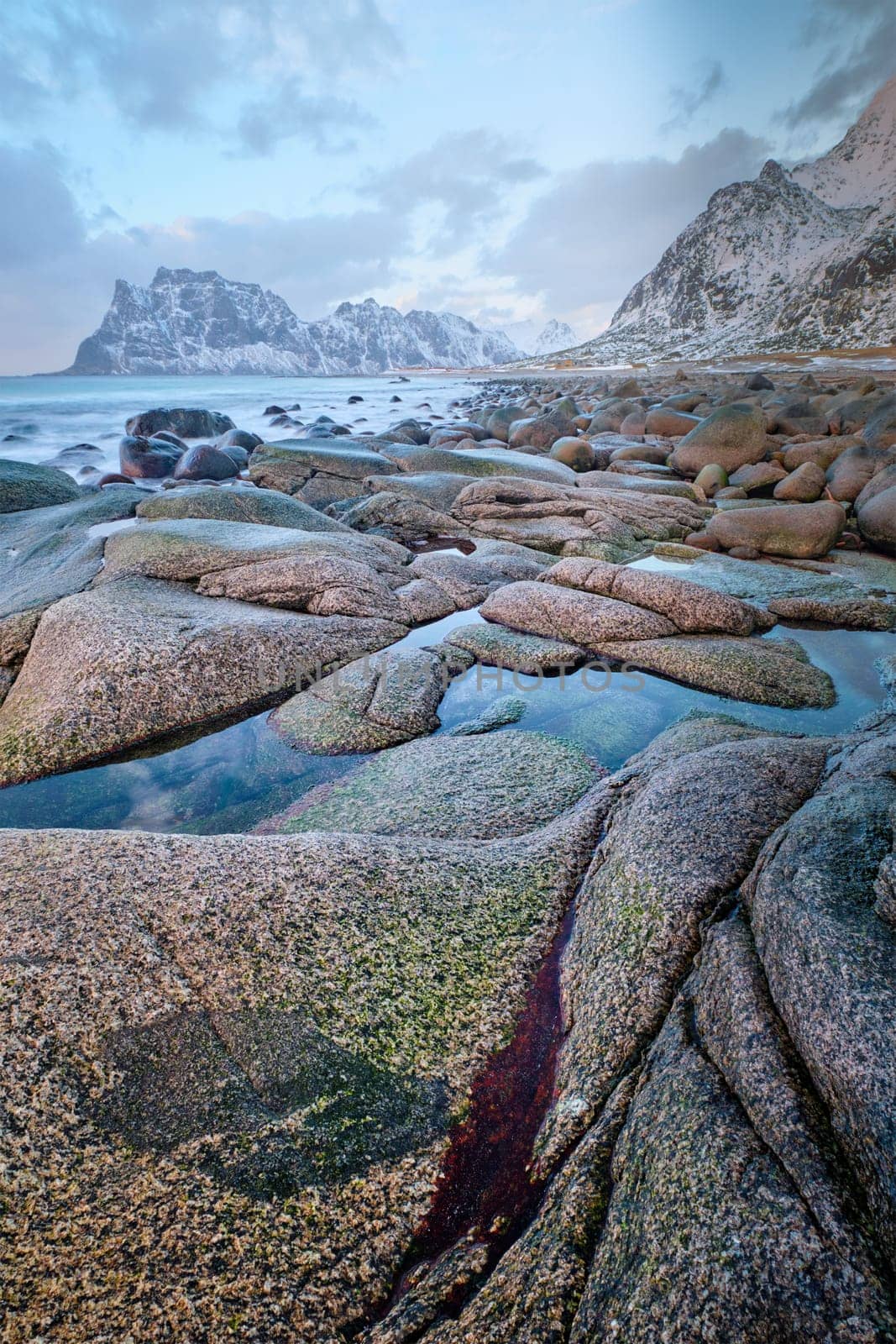 Rocks on beach of fjord of Norwegian sea in winter on sunset. Utakliev beach, Lofoten islands, Norway