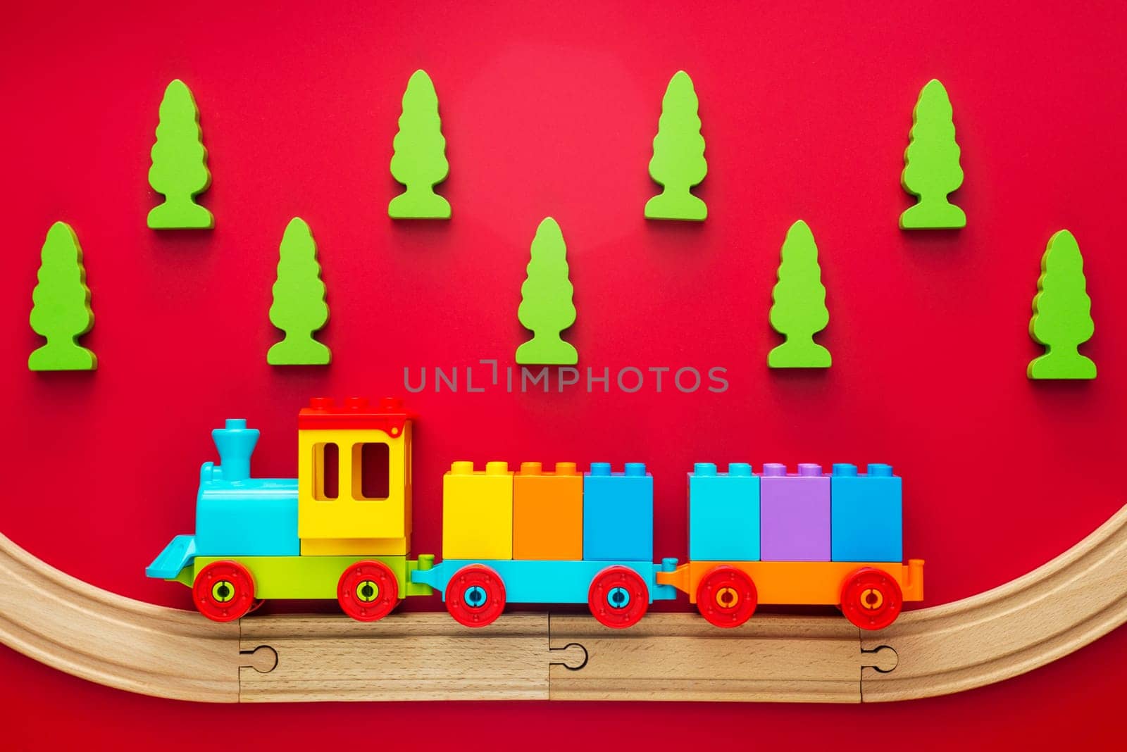 Colorful toy train on wooden railway with green trees on red background. Kids background.