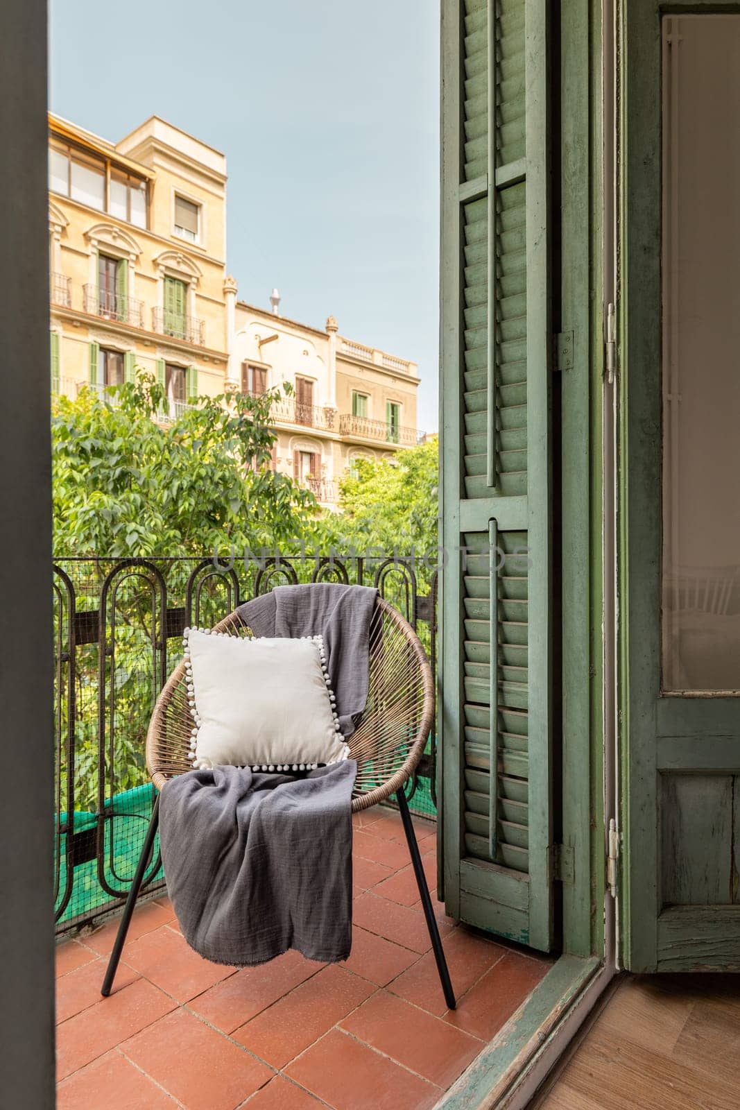 A sunny balcony with a wooden chair, traditional shutters, and trees. Cozy and inviting home.