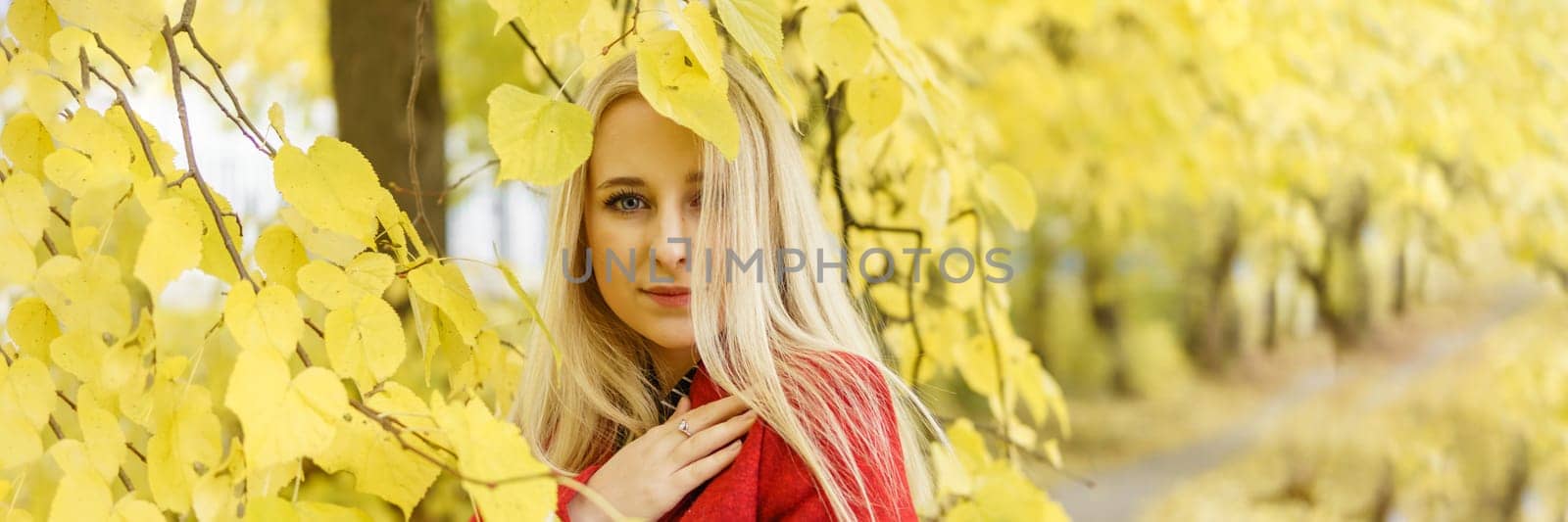 A young blonde woman walks around the autumn city in a red coat. The concept of urban style and lifestyle.