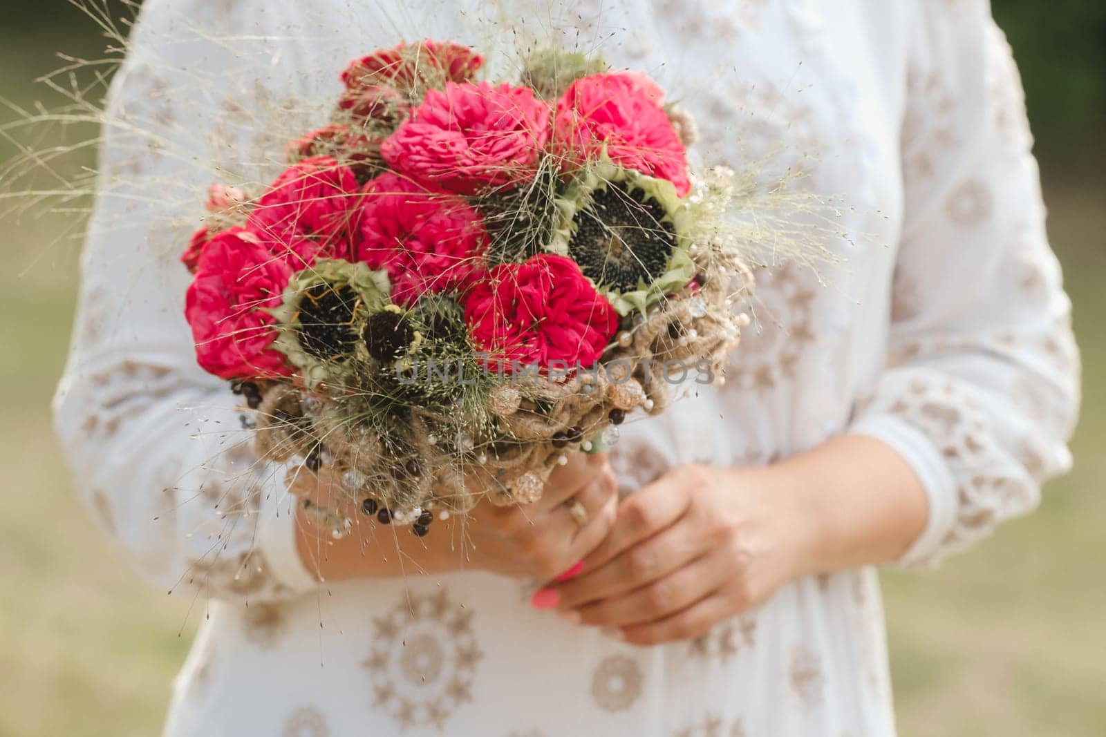 The bride holds her wedding bouquet with red peonies and sunflowers in her hands.