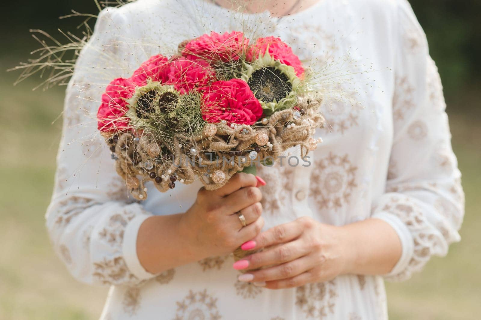 The bride holds her wedding bouquet with red peonies and sunflowers in her hands.