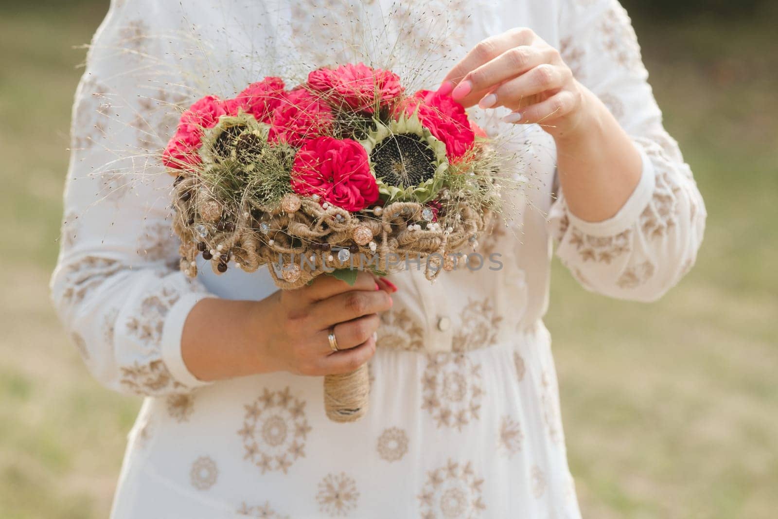 The bride holds her wedding bouquet with red peonies and sunflowers in her hands.