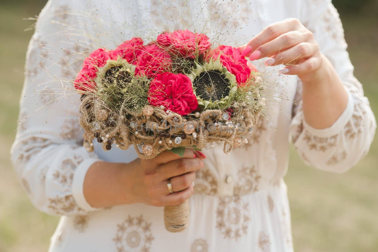 The bride holds her wedding bouquet with red peonies and sunflowers in her hands.