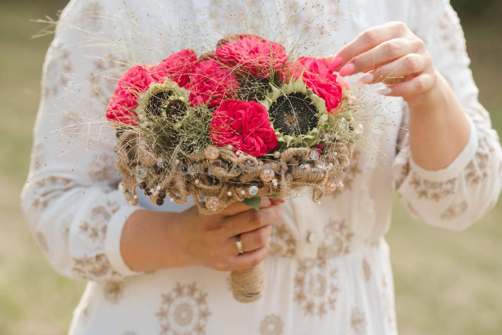 The bride holds her wedding bouquet with red peonies and sunflowers in her hands.