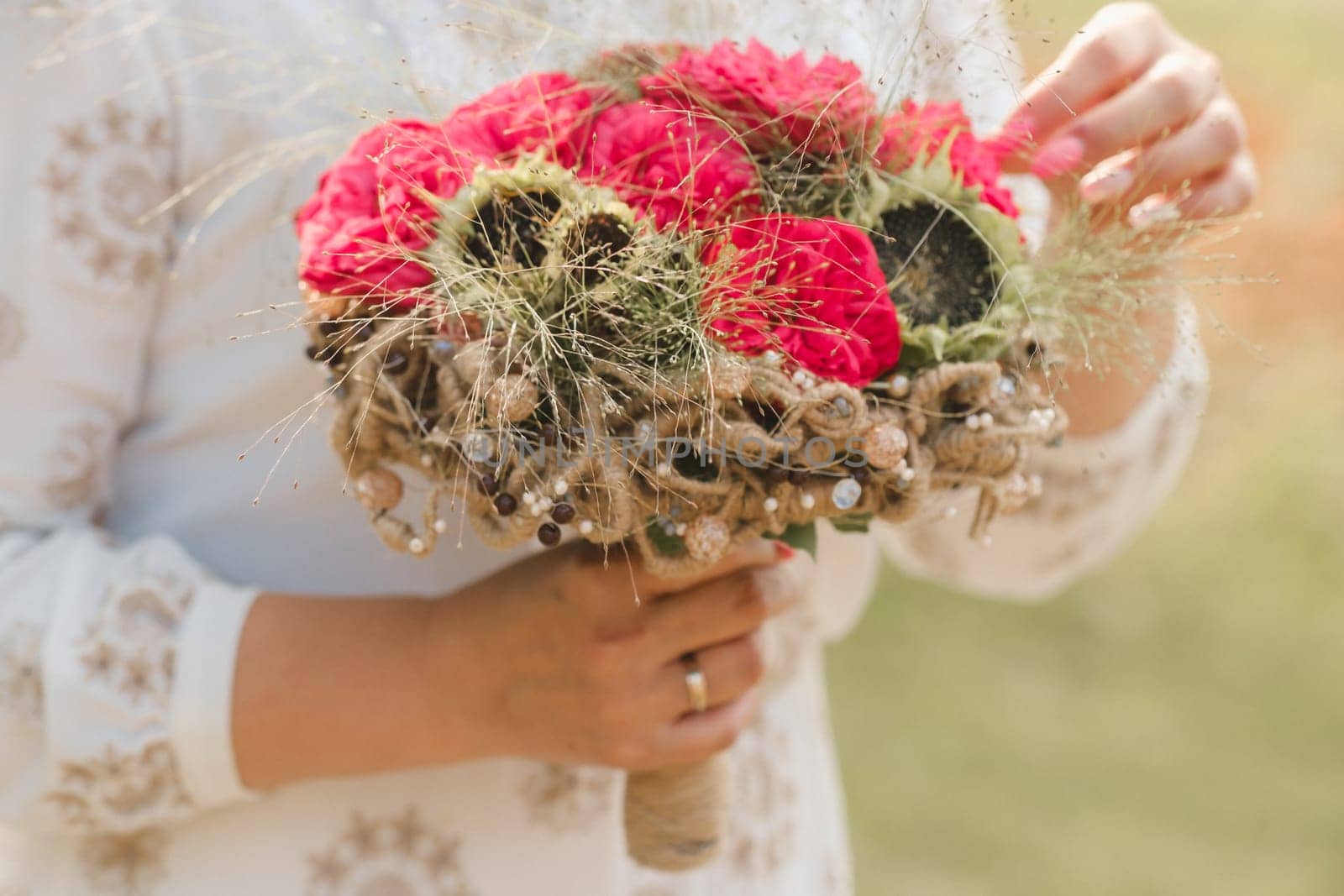 The bride holds her wedding bouquet with red peonies and sunflowers in her hands.