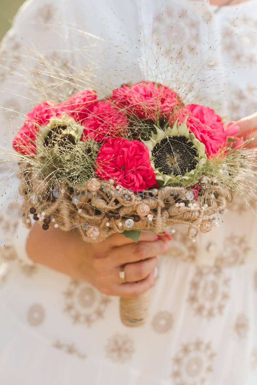 The bride holds her wedding bouquet with red peonies and sunflowers in her hands.