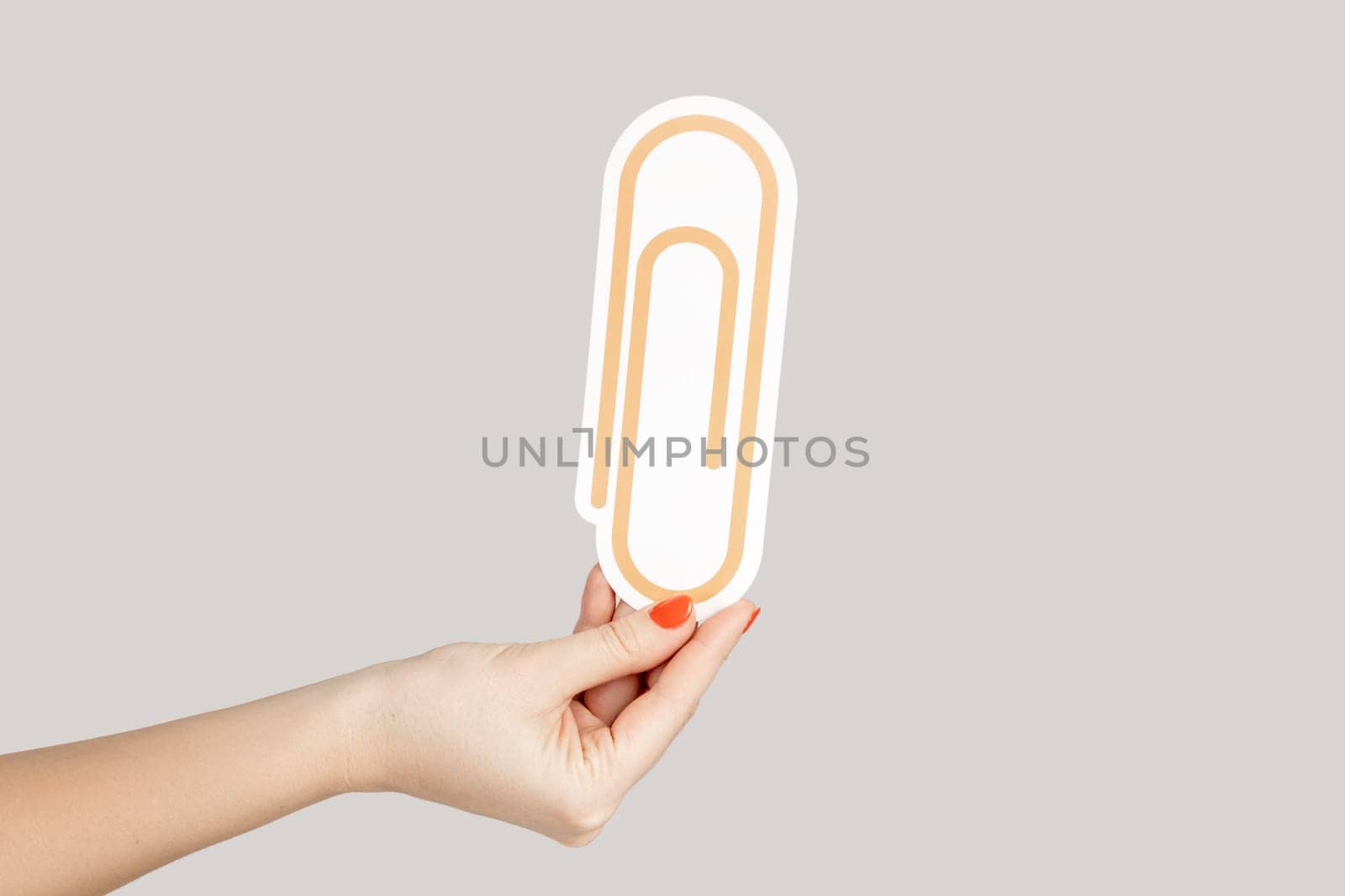 Closeup of woman hand showing paper craft clip, symbol of binding paper, office tools. Indoor studio shot isolated on gray background.