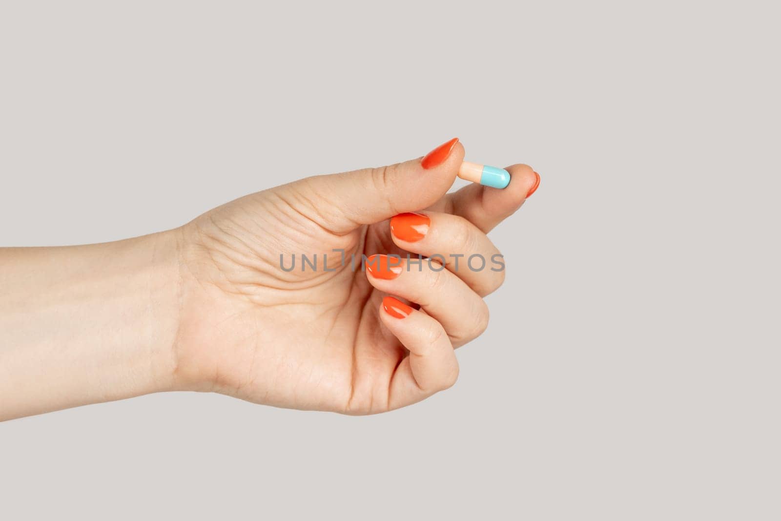 Closeup of woman hand showing herb capsule, nutritional supplement, vitamin pill, herbal medicine. Indoor studio shot isolated on gray background.