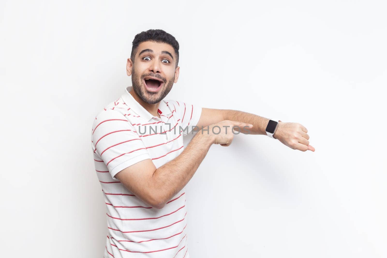Amazed positive optimistic man wearing striped t-shirt looking at camera, pointing at smart watch. by Khosro1