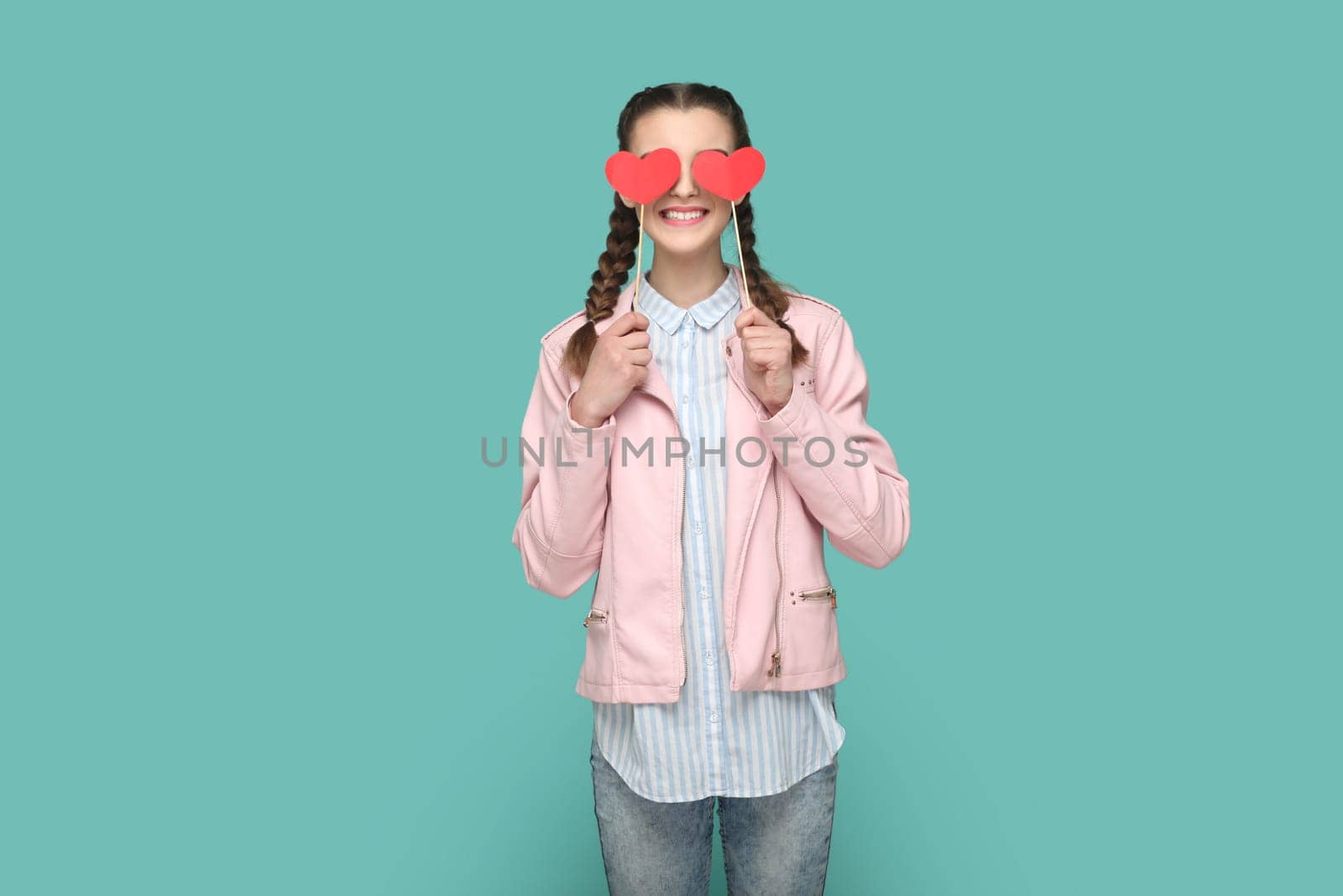 Romantic positive teenager girl with braids standing covering her eyes with two red hearts on stick. by Khosro1