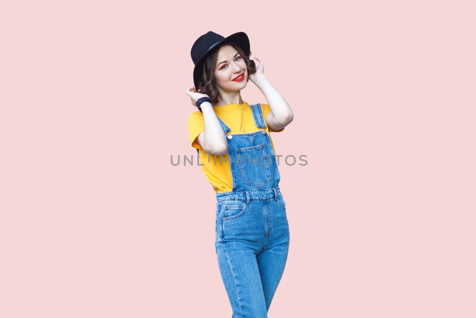 Charming hipster woman in blue denim overalls looking at camera with positive expression. by Khosro1