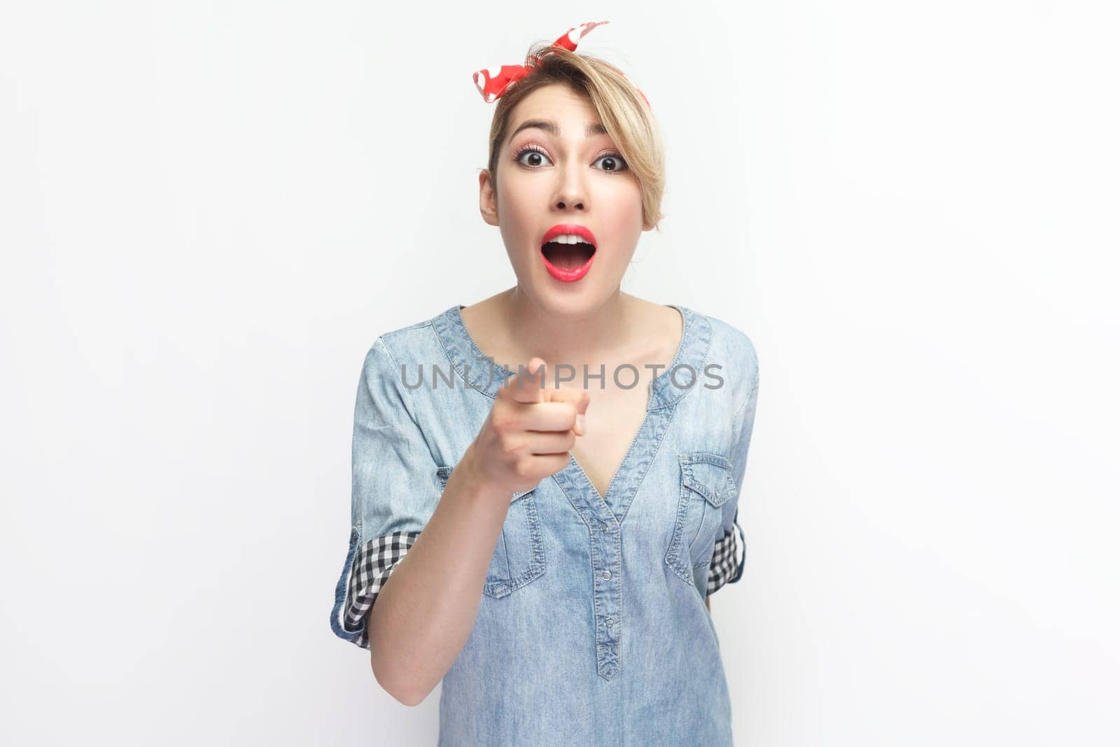 Surprised shocked blonde woman in red headband standing, pointing at you, looking with big eyes. by Khosro1