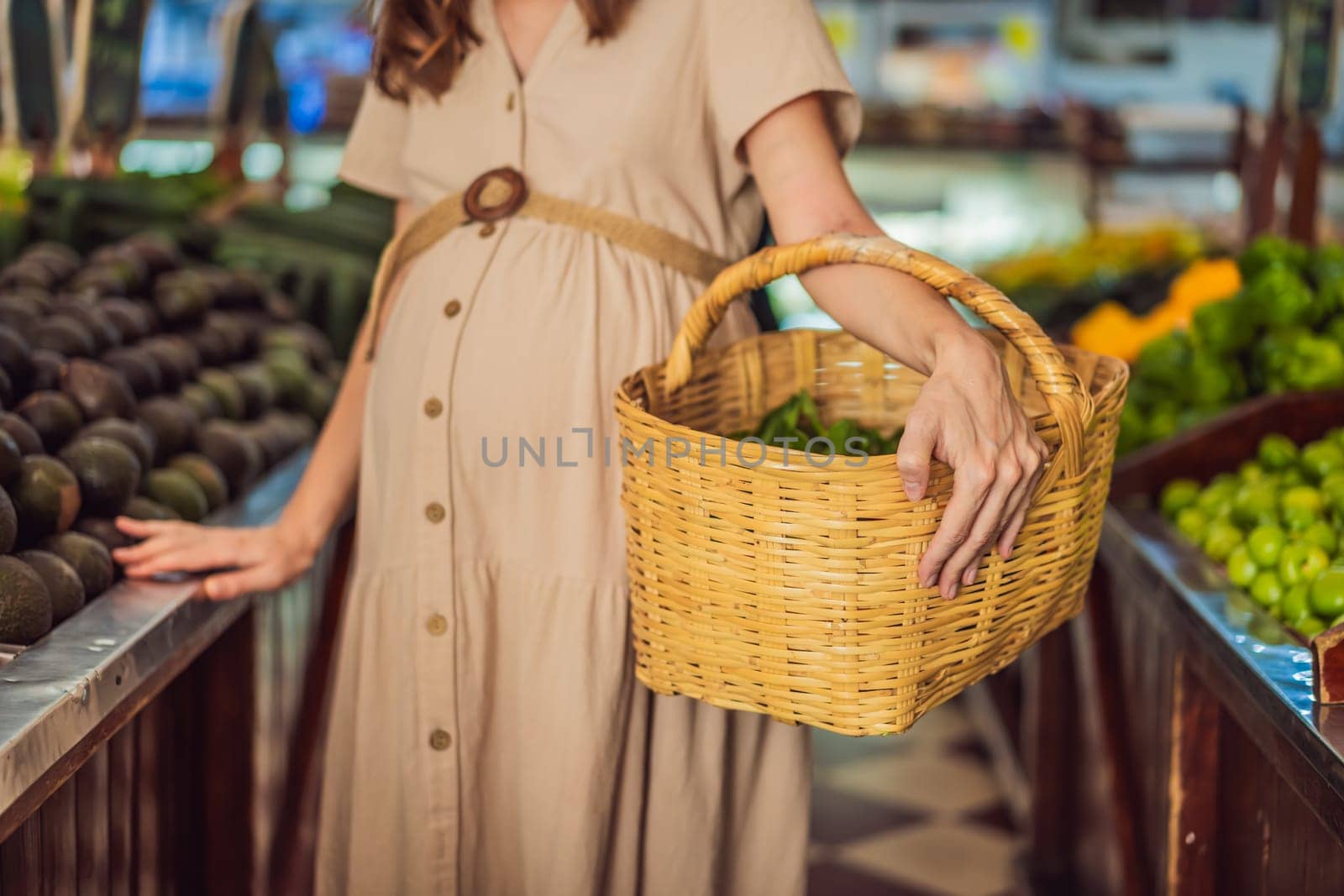 A glowing pregnant woman after forty makes a healthy choice as she selects organic vegetables and fruits at the vibrant organic market, prioritizing her well-being and her baby's health.