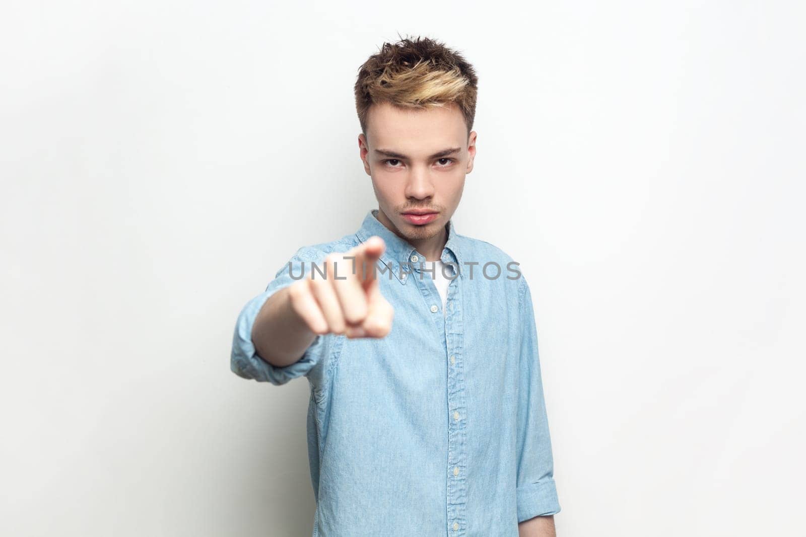 Portrait of bossy strict man wearing denim shirt looking and indicating to camera, choosing you, you have problems, has serious expression. Indoor studio shot isolated on gray background.