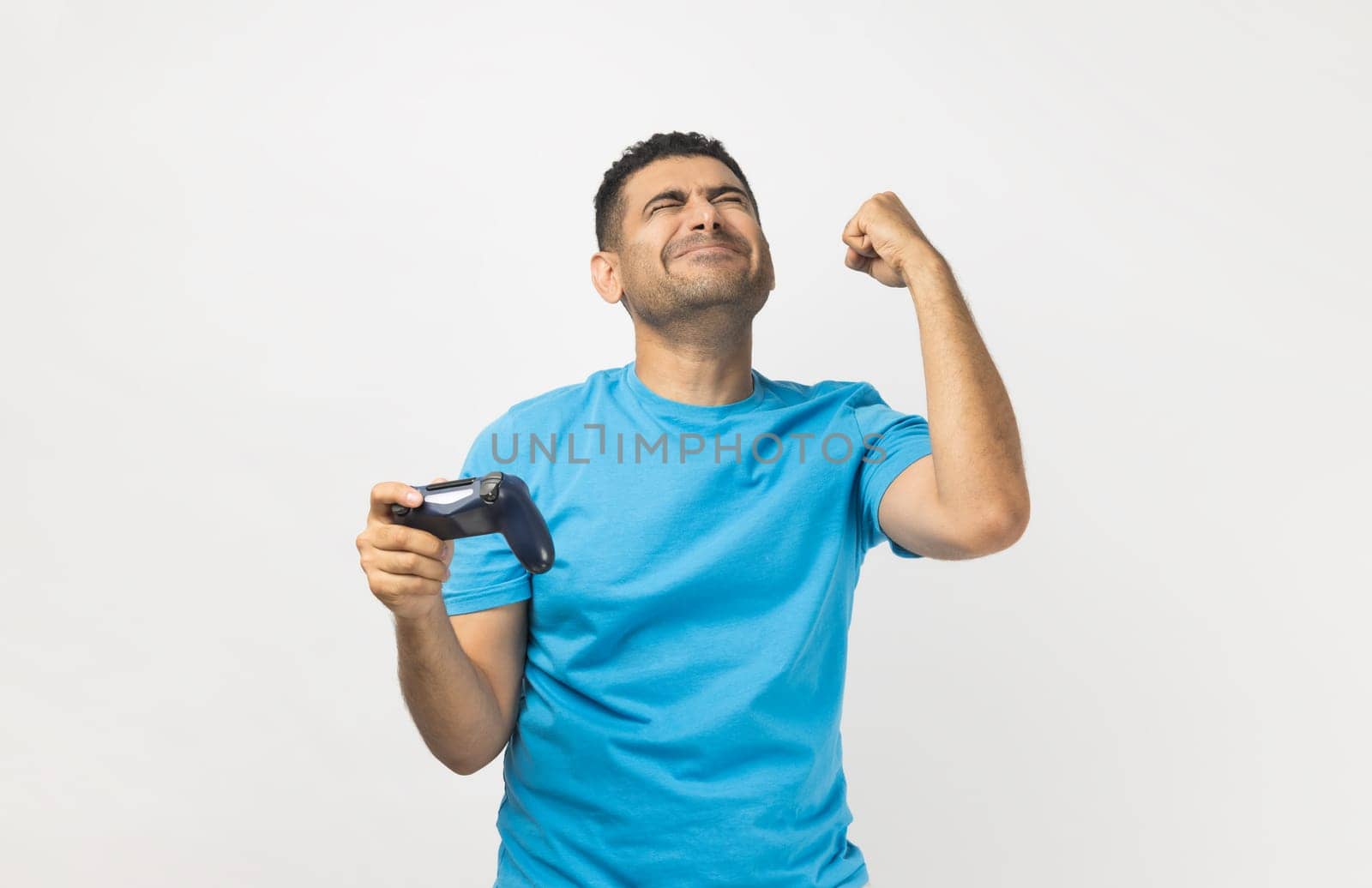 Cheerful man gamer playing video games, holding joystick and clenched fist, celebrating his winning. by Khosro1