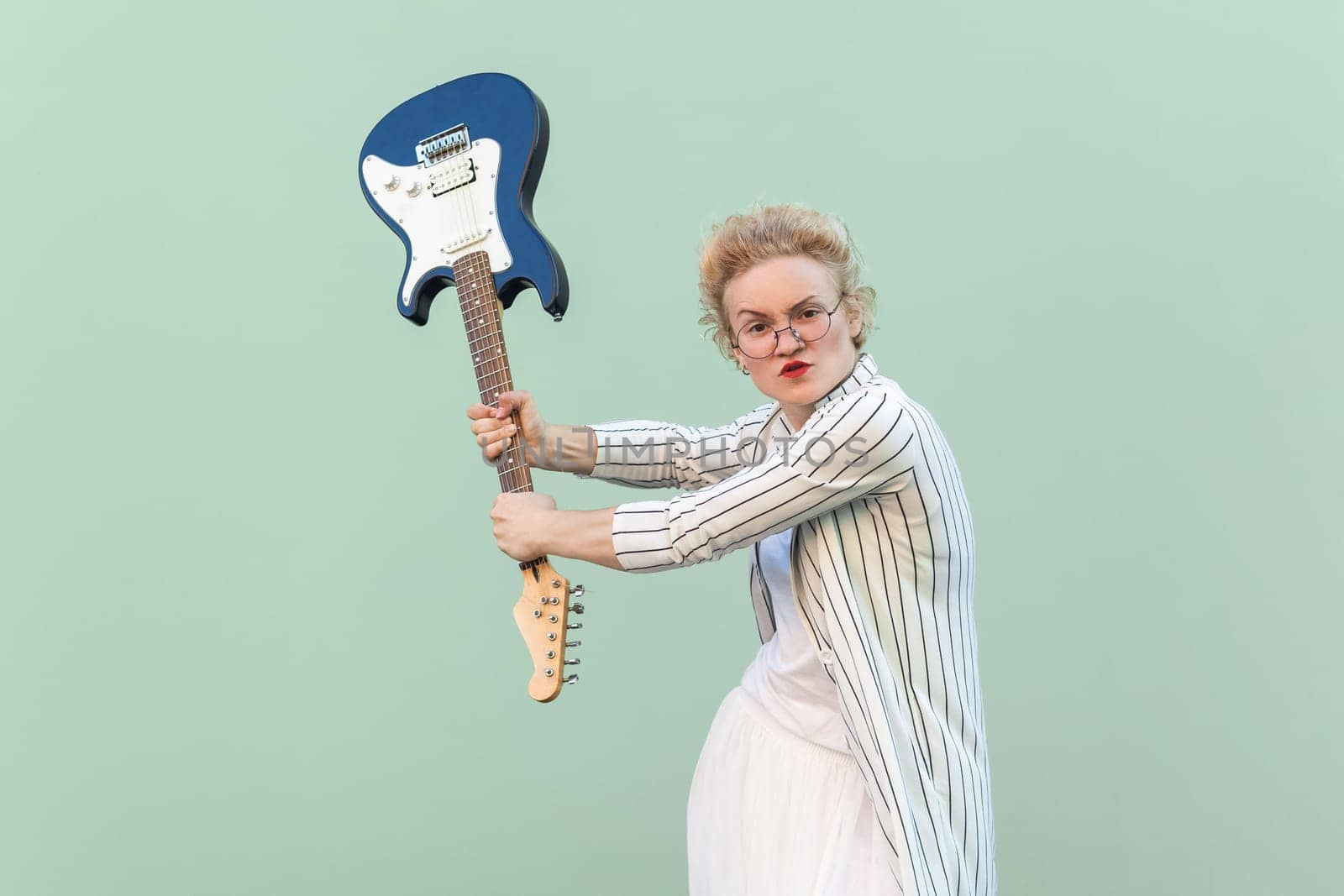 Angry woman in white striped blouse with eyeglasses standing, holding electric guitar and attacking. by Khosro1