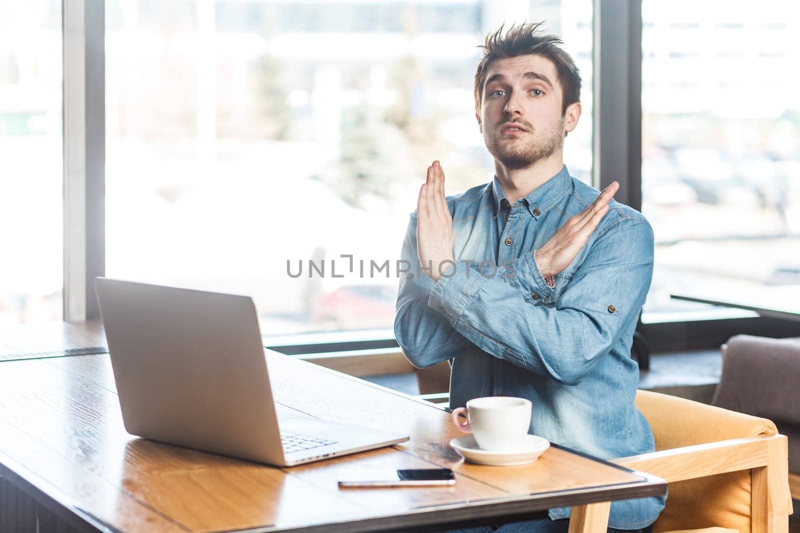 Serious handsome man freelancer working on laptop, showing x sign, no way gesture, looking at camera by Khosro1