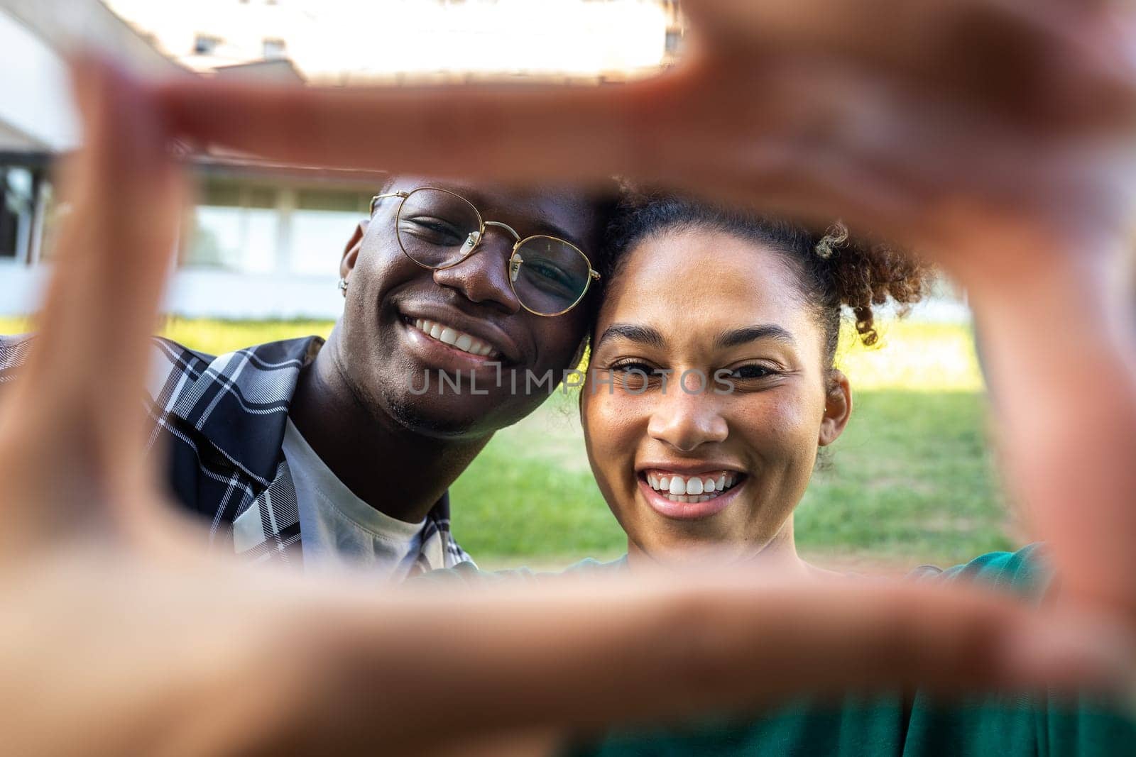 Happy, smiling young African American couple making frame with fingers looking at camera. Loving relationship by Hoverstock