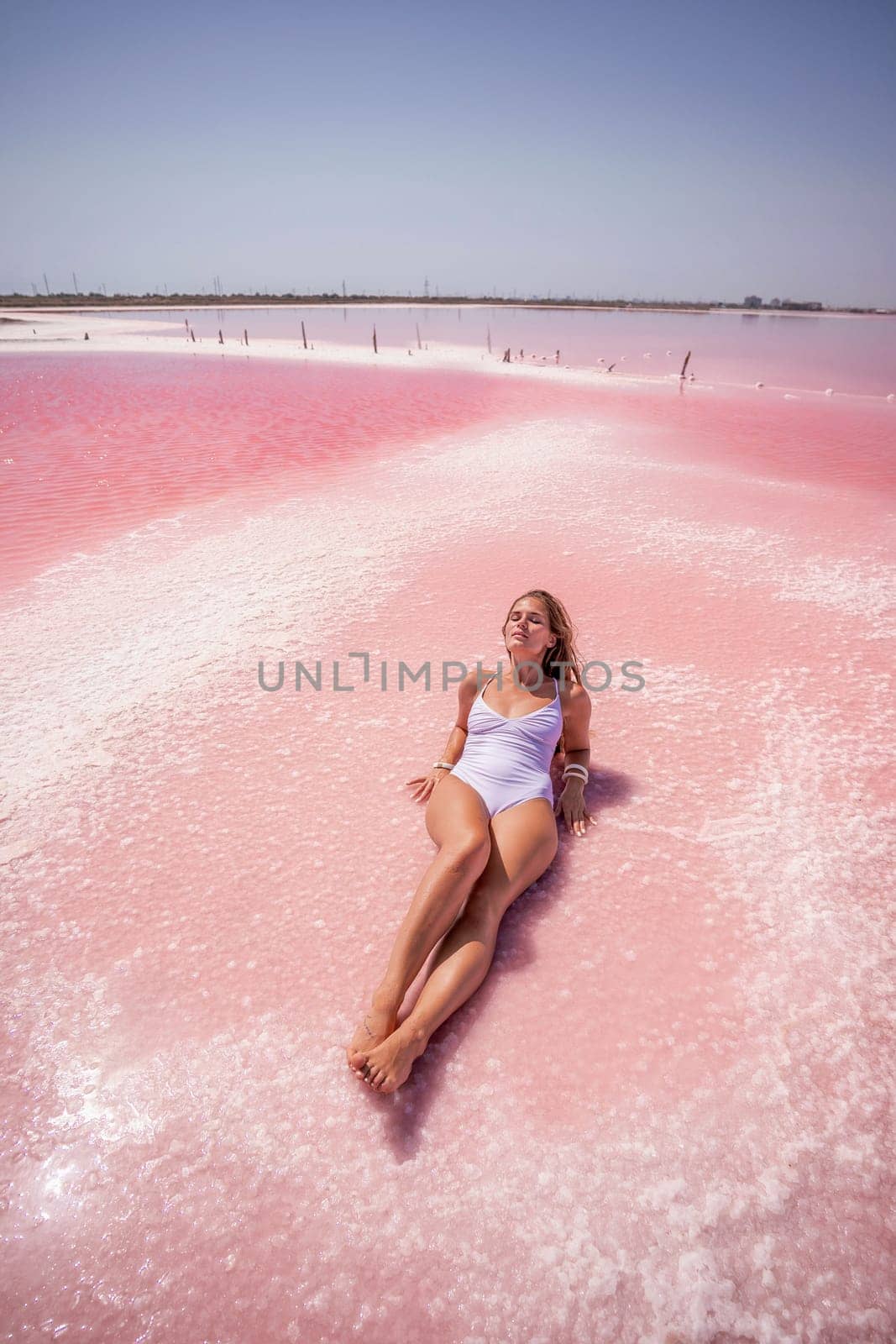 Woman pink salt lake. She lies in a white bathing suit. Wanderlust photo for memory.