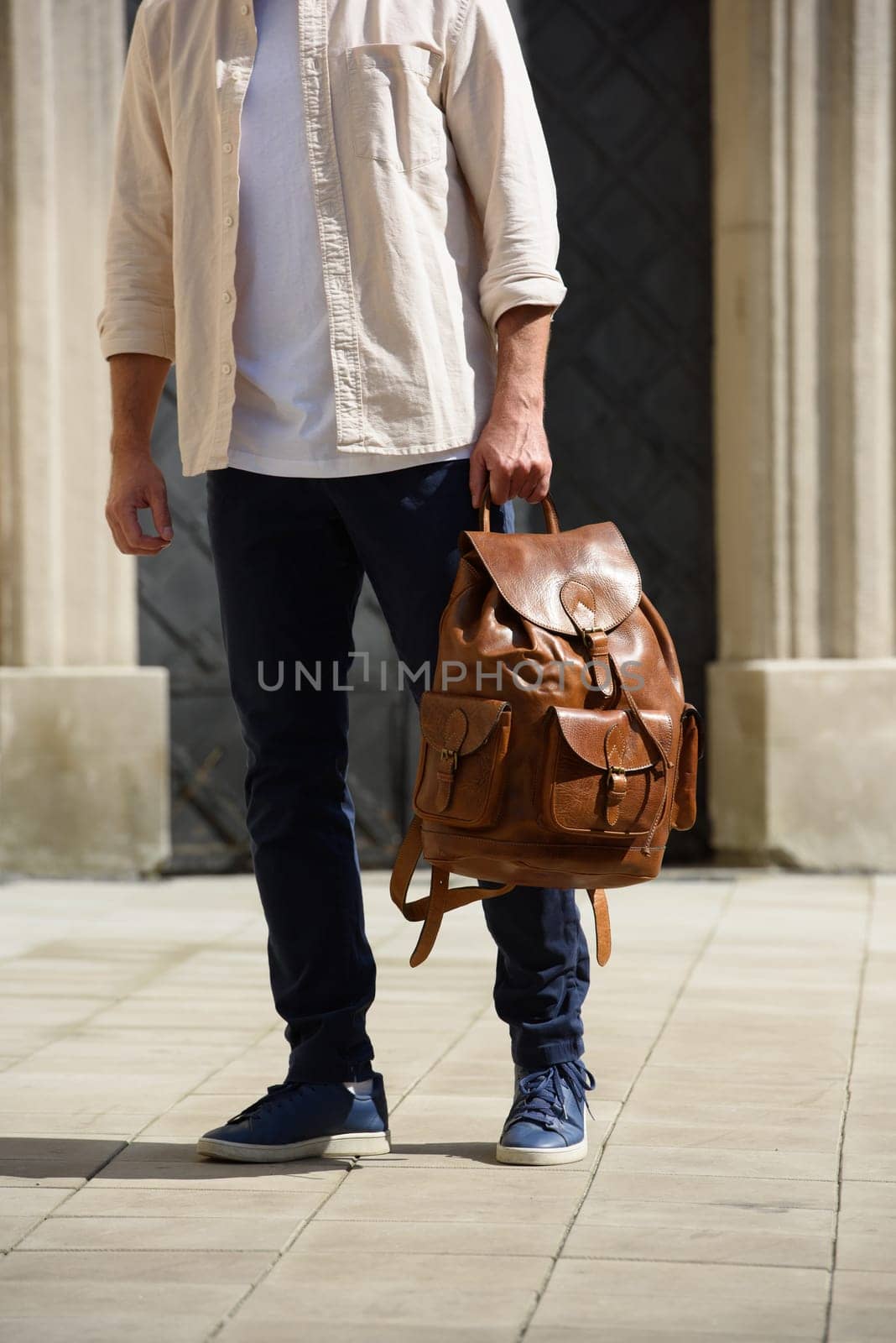 Handsome businessman walking on the street, with luxury leather backpack. Man wearing blue pants, sneakers, white t-shirt and beige shirt