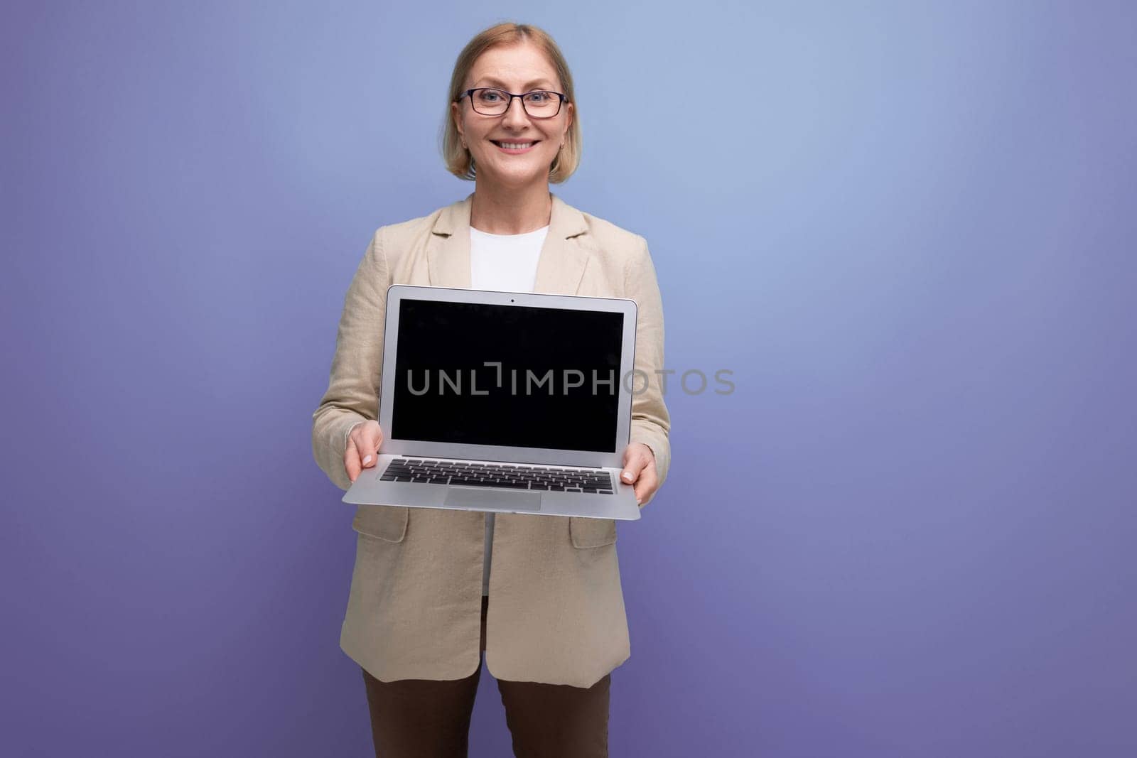 successful 50s middle aged woman in jacket with laptop to work on studio background with copy space.