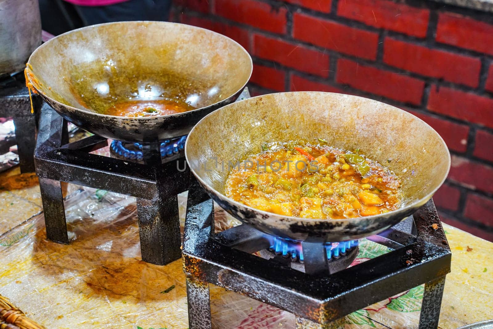 Food being prepared on simple gas stoves in typical Pakistani restaurant, herbs and spices dropped into steel pan with hot dish, closeup detail.
