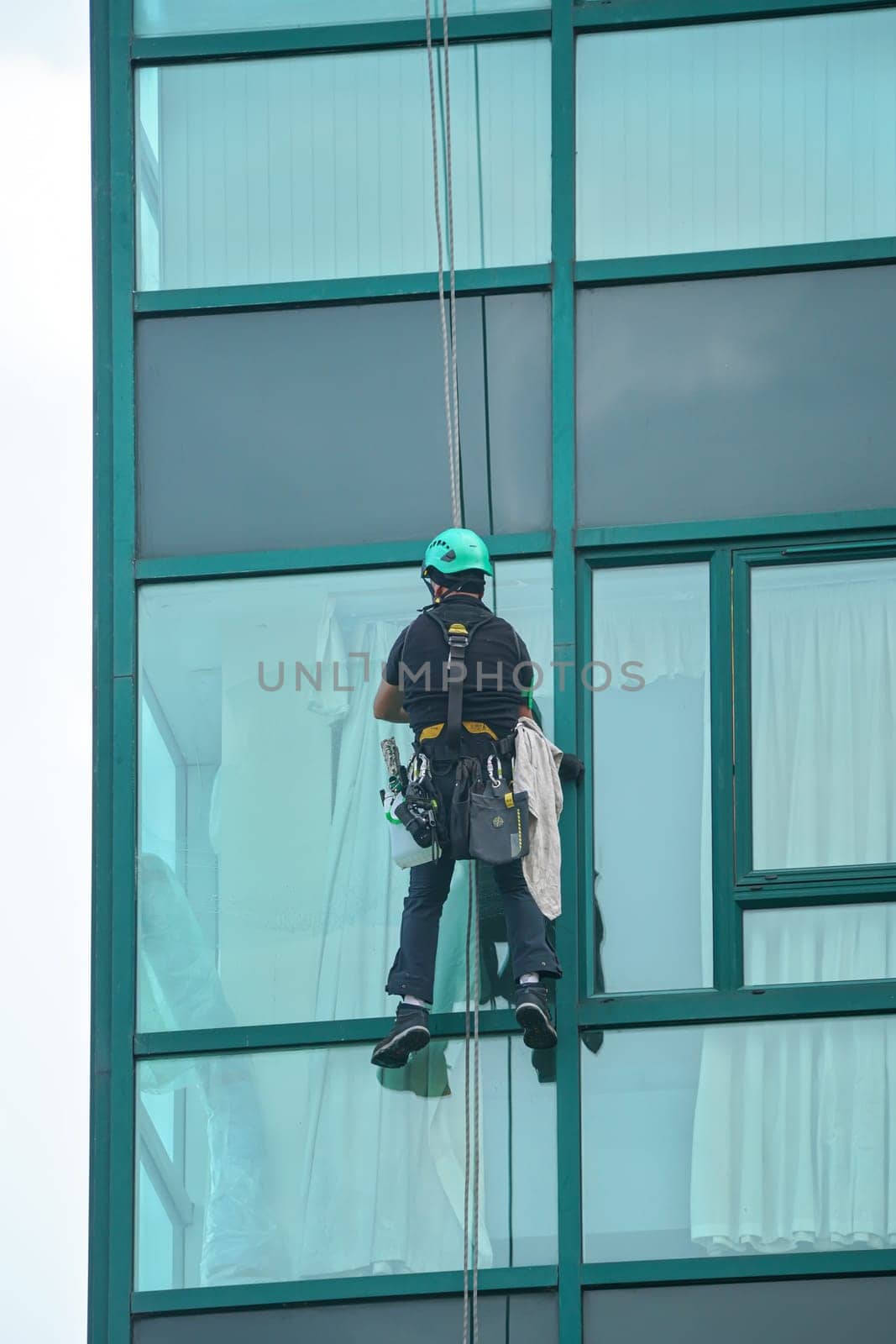 Industrial window cleaner - man hanging on roofs with safety equipment, cleaning facade of tall modern glass building by Ivanko