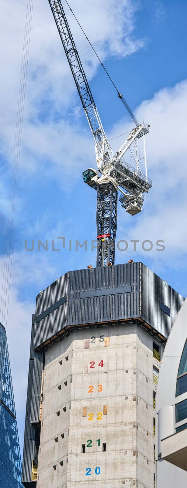 Tall modern skyscraper construction, concrete walls with numbers marking floors to be built, large industrial crane on top.