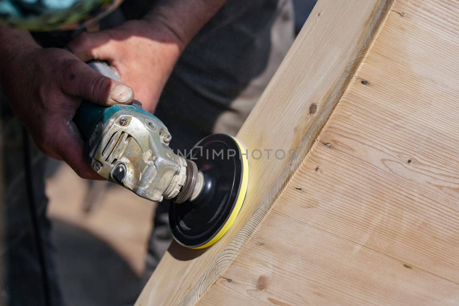 Man polishing wooden chest with old angle grinder during sunny day, closeup detail to hands without gloves.