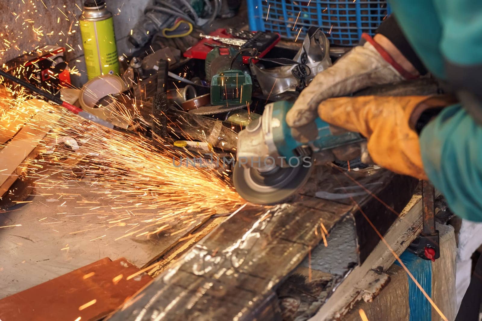 Man working with rotary angle grinder at workshop, closeup detail, orange sparks flying around.