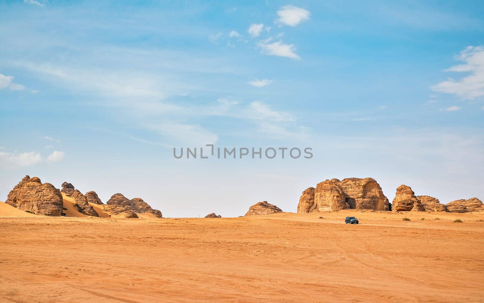 Typical desert landscape in Alula, Saudi Arabia, sand with some mountains, small offroad vehicle, local man and camels at distance.