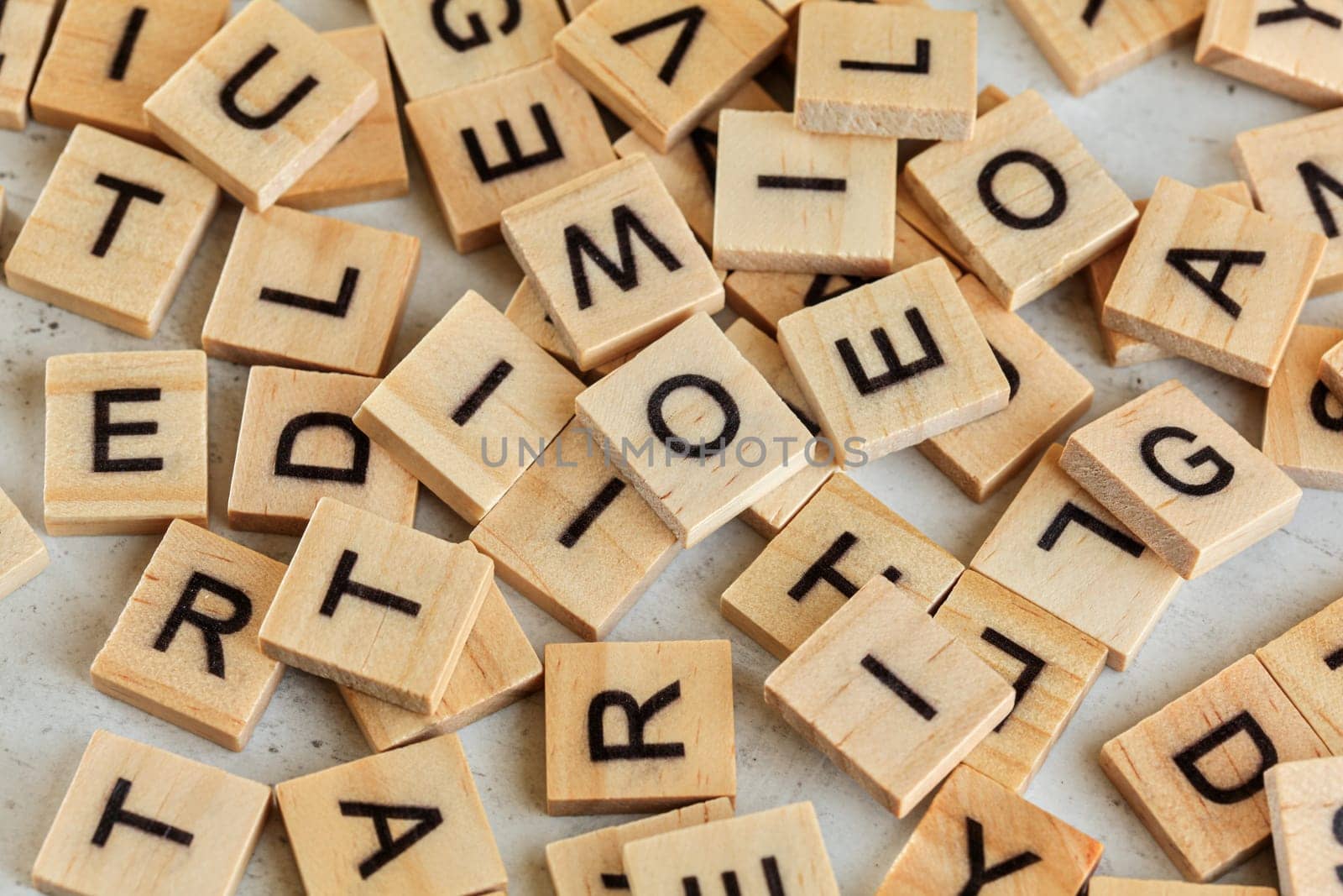 Pile of wooden tiles with various letters scattered on white stone like board, closeup view from above.