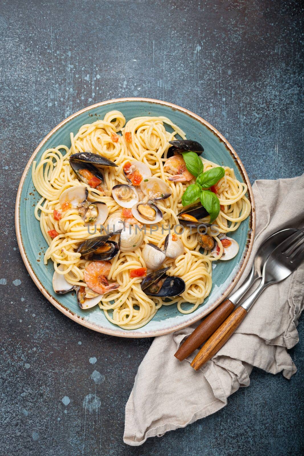 Italian seafood pasta spaghetti with mussels, shrimps, clams in tomato sauce with green basil on plate on rustic blue concrete background overhead. Mediterranean cuisine