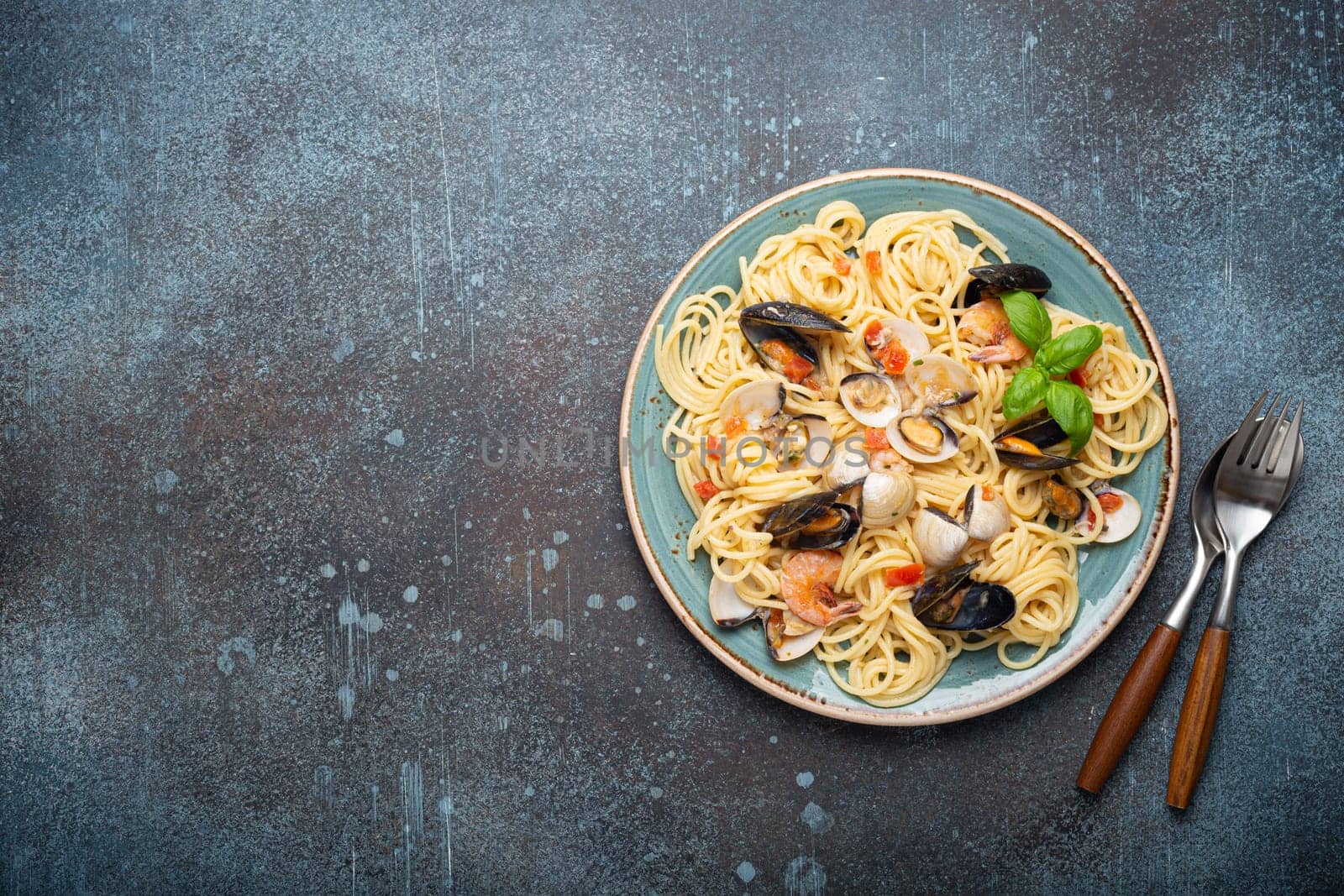 Italian seafood pasta spaghetti with mussels, shrimps, clams in tomato sauce with green basil on plate on rustic blue concrete background overhead. Mediterranean cuisine, space for text