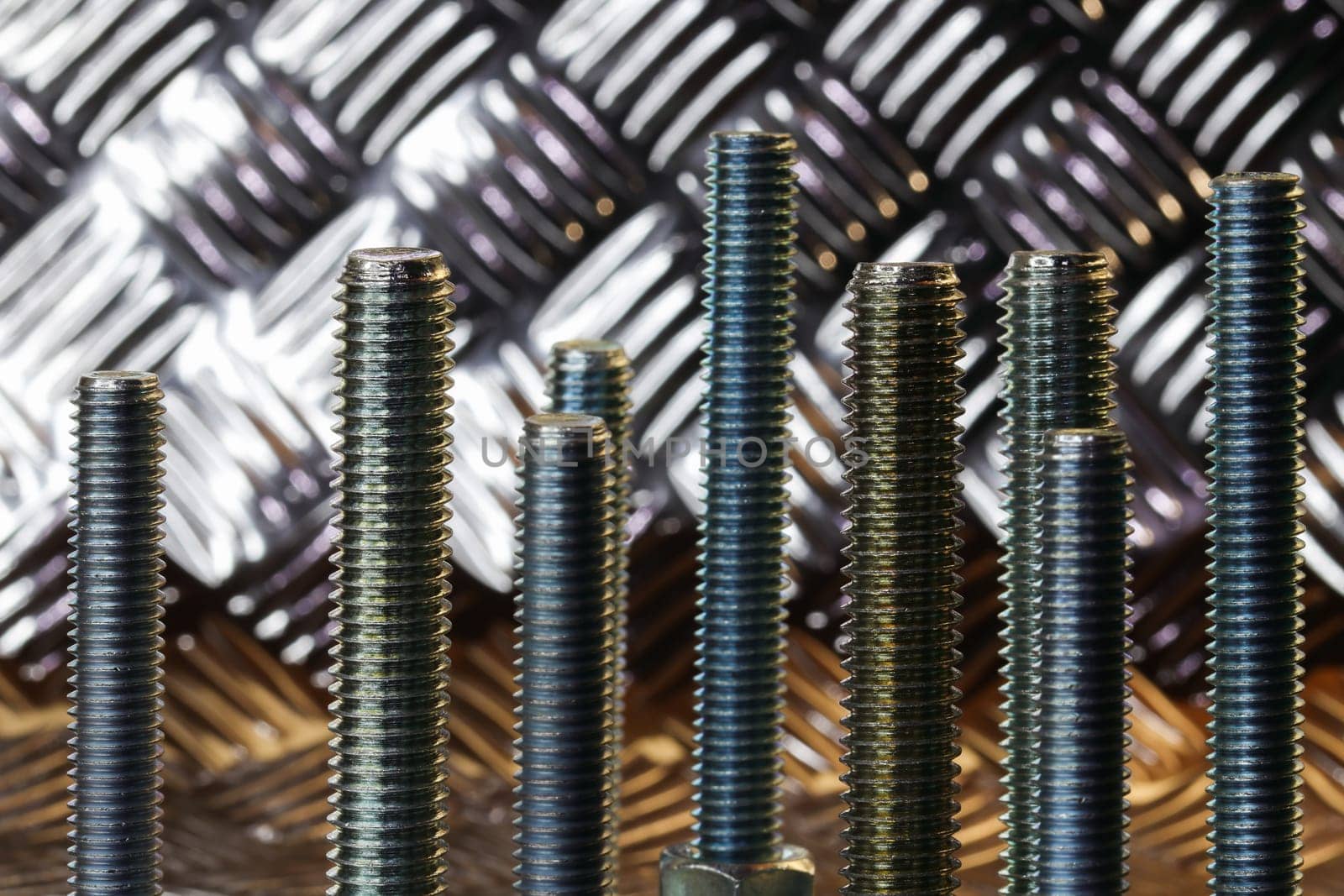 Different sizes of threaded steel bolts standing erect with tread plate backdrop