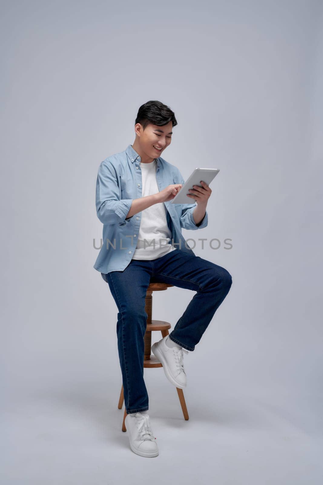 Handsome attractive smiling happy young male using tablet and sitting on the chair  by makidotvn