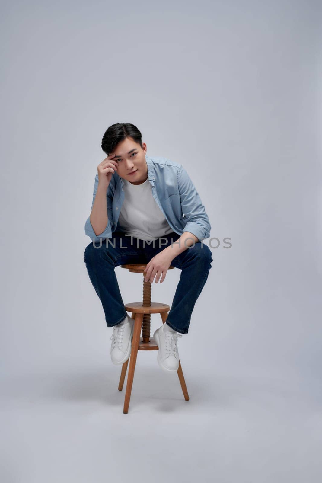 Full length of handsome young man looking at camera with smile while sitting against white background