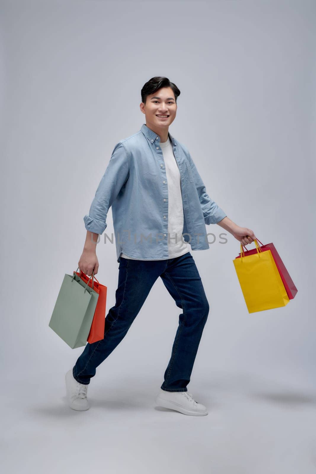 A portrait of happy young asian man holding shopping bags, full body by makidotvn