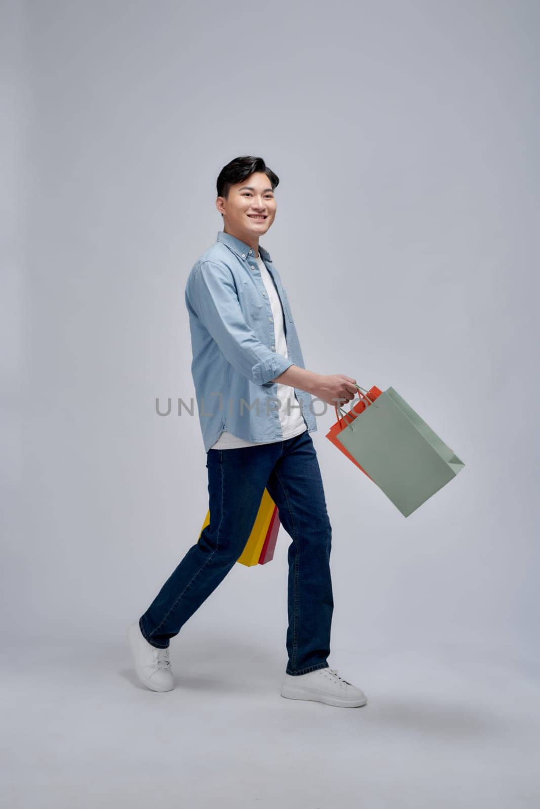 Young positive man hold bags from shopping store advert satisfied by makidotvn