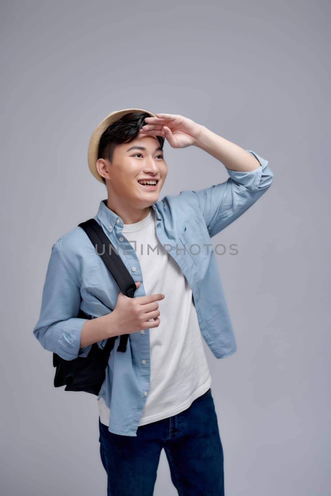Seaching for adventure, studio portrait of young man in hat holding hand on forehead by makidotvn