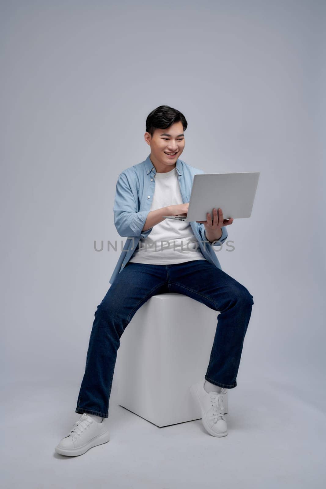 Young Asian man sitting and using laptop on white background