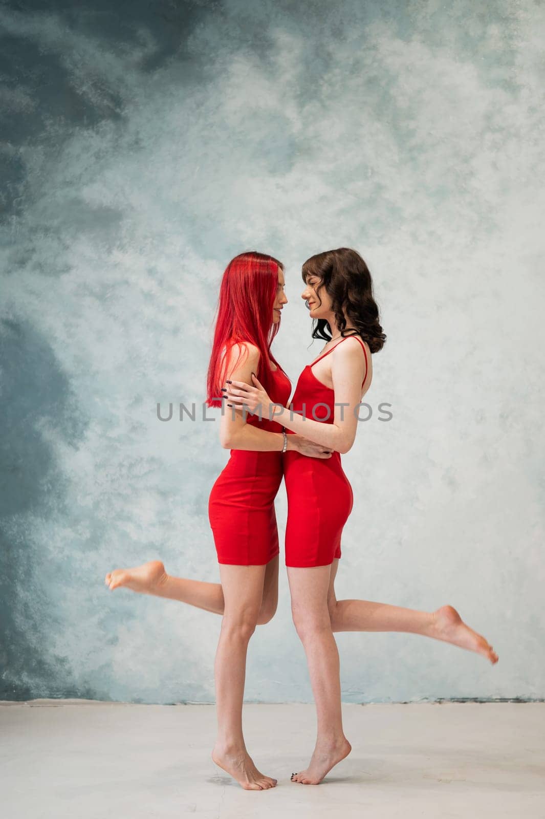 Full-length portrait of two tenderly embracing women dressed in identical red dresses. Lesbian intimacy. by mrwed54