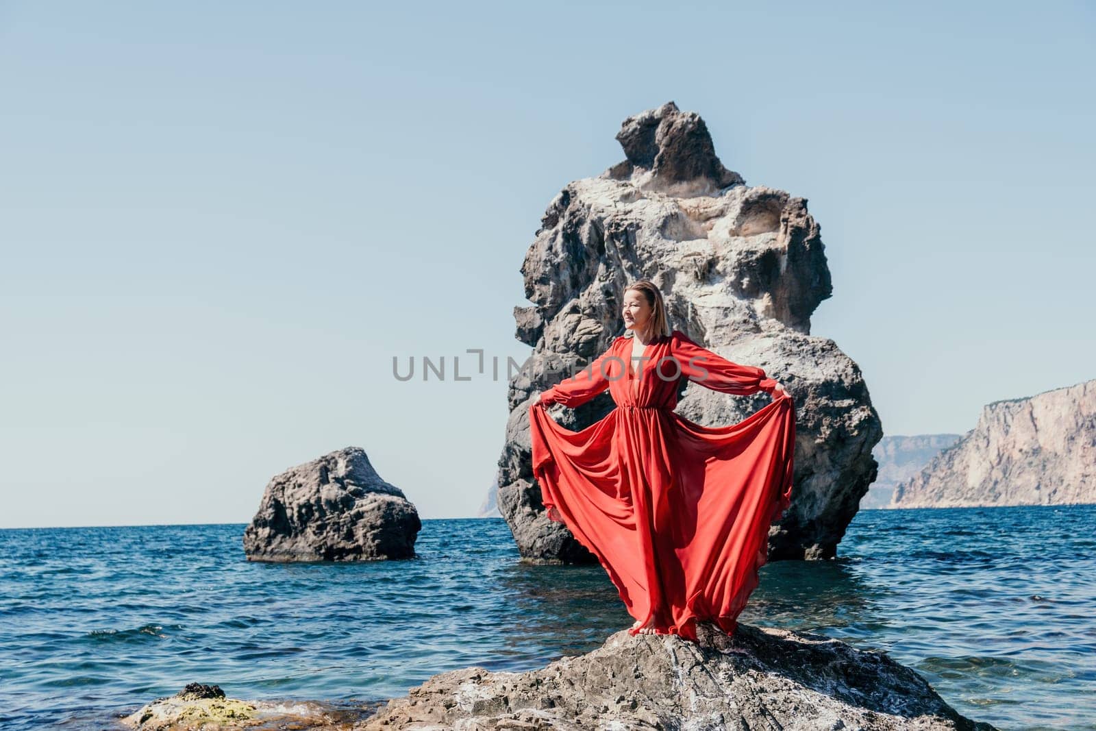 Woman travel sea. Happy tourist in long red dress enjoy taking picture outdoors for memories. Woman traveler posing on beach at sea surrounded by volcanic mountains, sharing travel adventure journey by panophotograph