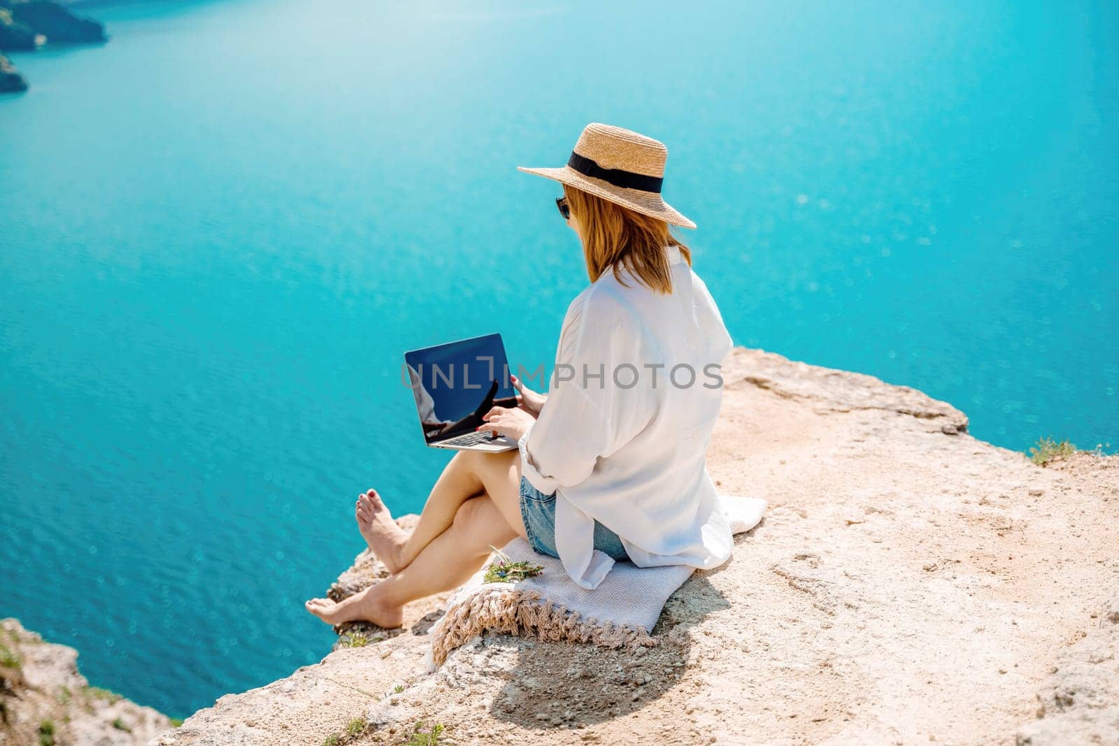 Freelance woman working on a laptop by the sea, typing away on the keyboard while enjoying the beautiful view, highlighting the idea of remote work. by Matiunina