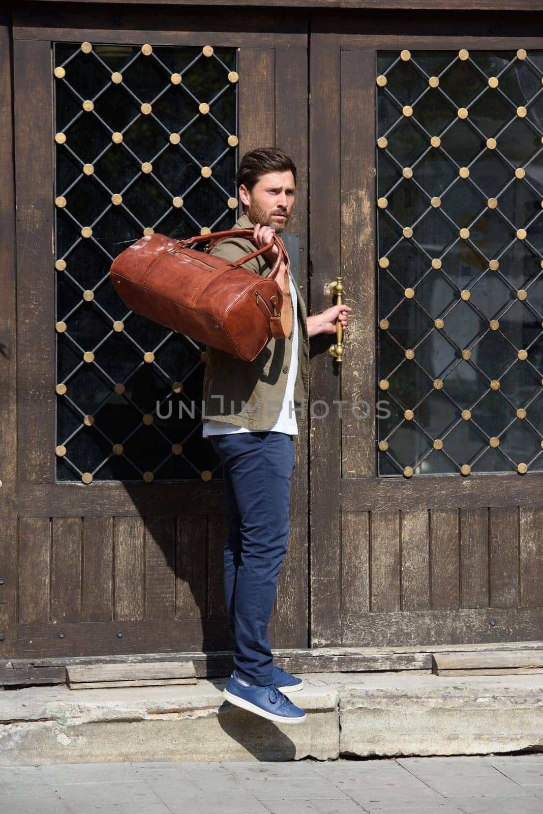 a man with a bag. black leather travel bag, street photo. man is wearing blue sneakers, jeans, a white T-shirt and a jacket by Ashtray25